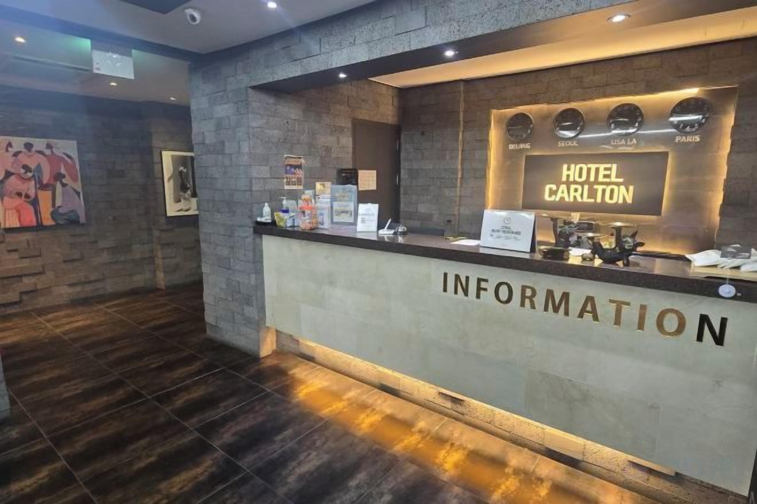 A reception desk with a sign reading 'HOTEL CARLTON' and a wall-mounted information board.