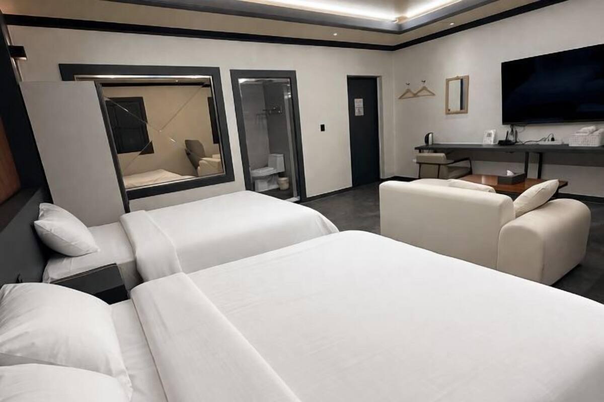 Quarto de hotel com duas camas, um sofá, uma escrivaninha, uma televisão e uma casa de banho.