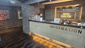 En hotellobby med modern design, med en receptionsdisk där det står "HOTEL CARLTON" och "INFORMATION".