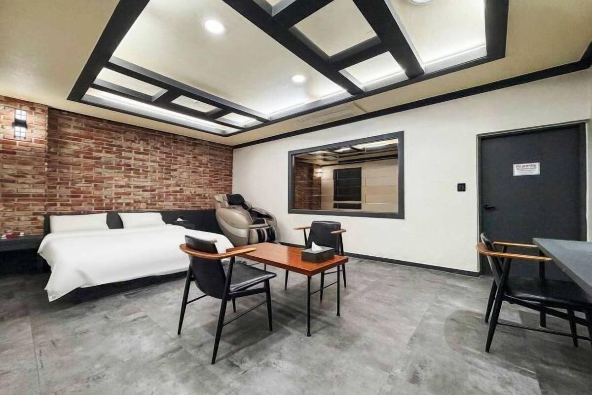 Quarto moderno com cama, escrivaninha e cadeira, parede de tijolos e claraboia.