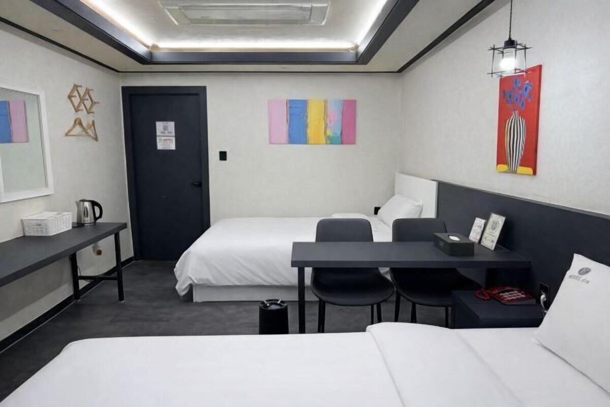 A hotel room with a bed, a desk, two chairs, a small table, a coffee maker, and artwork on the walls.