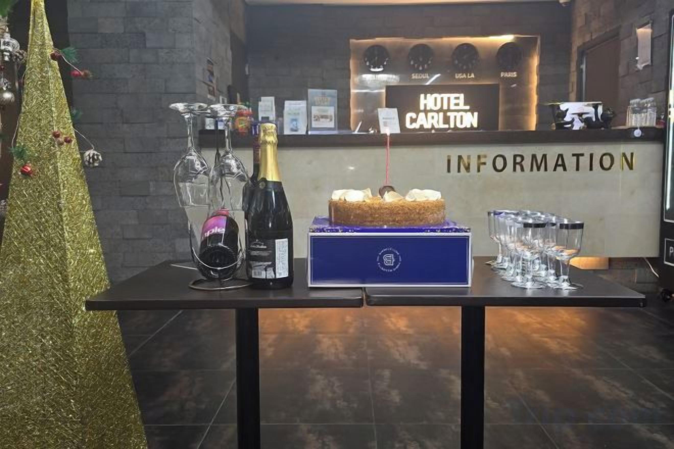 A reception desk with a sign reading 'HOTEL CARLTON INFORMATION' and a table with a cake, champagne, and glasses.
