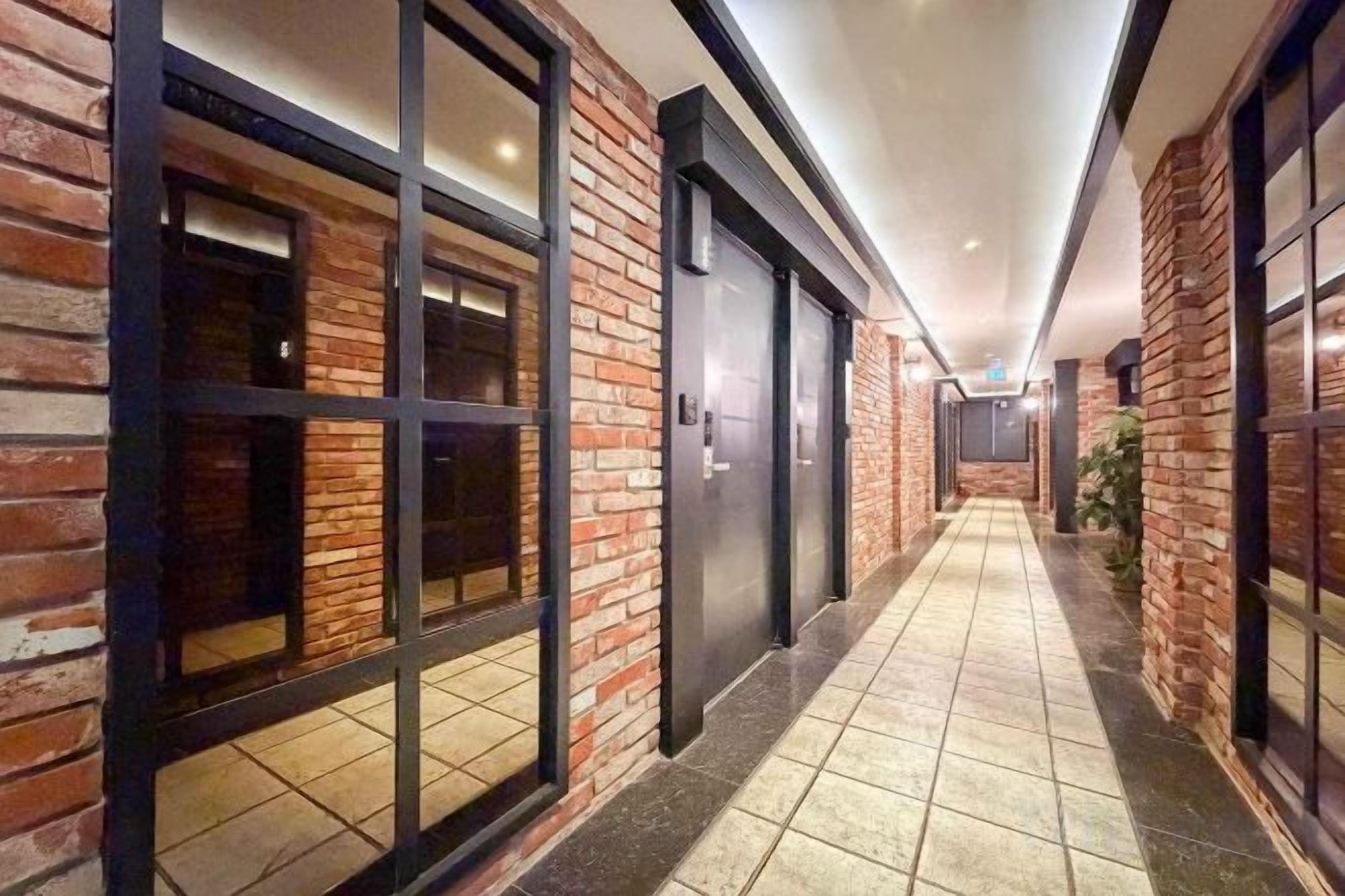 A corridor with brick walls, large windows, and a tiled floor.