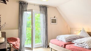 Une chambre à coucher comprenant un lit, une chaise, un bureau, un radiateur et une fenêtre avec des rideaux.