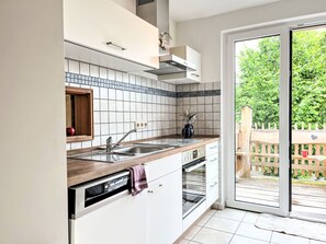Une cuisine moderne dotée d’un four encastré, d’un lave-vaisselle et d’une grande fenêtre donnant sur un jardin.
