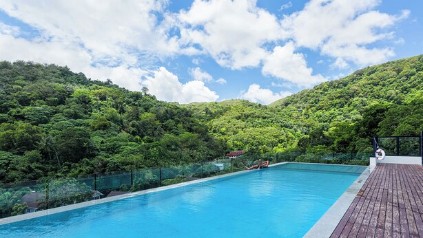 A swimming pool with a wooden deck, surrounded by lush green hills and a clear sky.