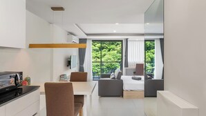 A modern hotel room with a kitchenette, a dining area, and a seating area with a view of greenery.