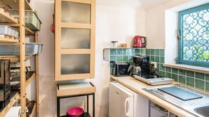 A compact kitchen with a wooden cabinet, a coffee maker, and a window with decorative iron bars.