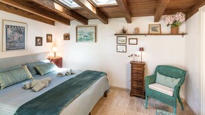 A cozy bedroom with a bed, a chair, a nightstand, and a shelf with decorative items.