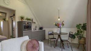 Espaço compacto com cozinha americana, área de refeições com duas cadeiras, sofá com almofadas decorativas e um vaso de planta.