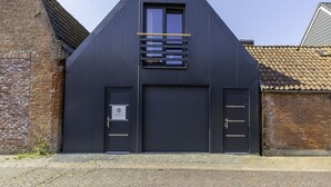 Edifício moderno com fachada escura, uma porta de garagem grande e uma pequena janela com persianas horizontais.