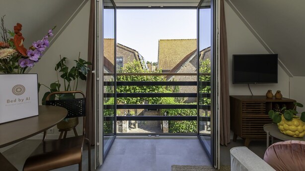 Um apartamento moderno com uma grande porta de vidro deslizante que dá para uma varanda, área de jantar com mesa e cadeiras, televisão de tela plana na parede e uma pequena planta em uma mesa lateral.