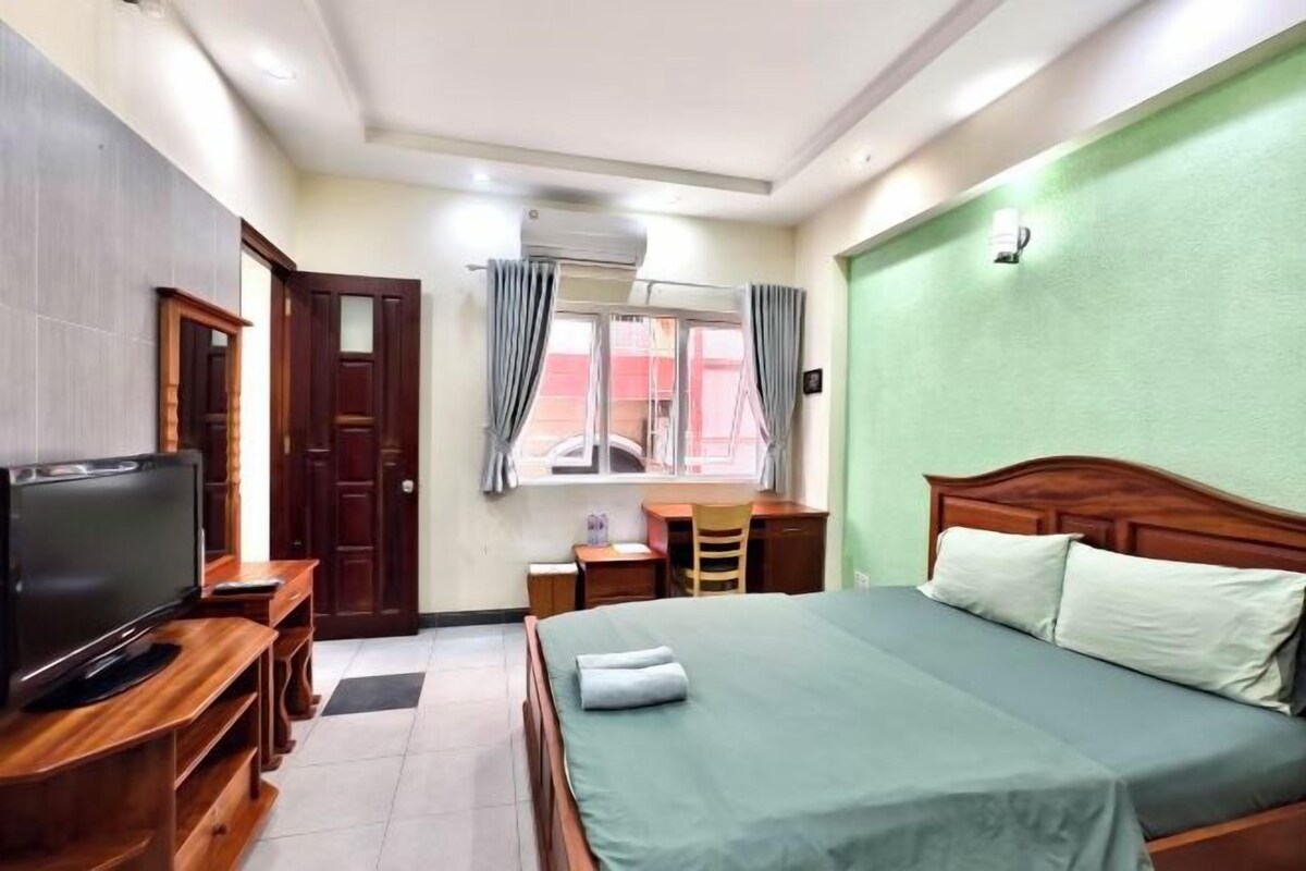 A hotel room with a bed, a TV, a desk, and a window with curtains.