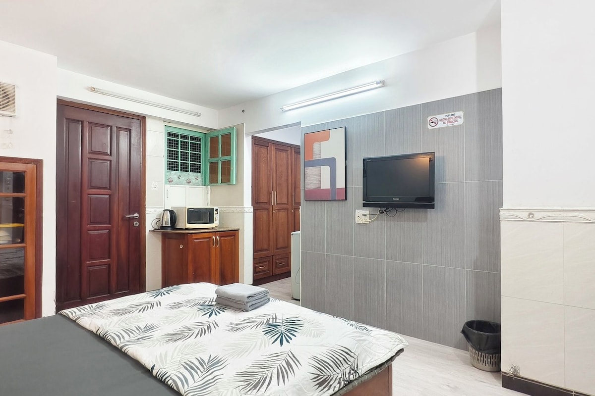 Une chambre de taille réduite comprenant un lit, un four à micro-ondes, une télévision et un petit coin cuisine.
