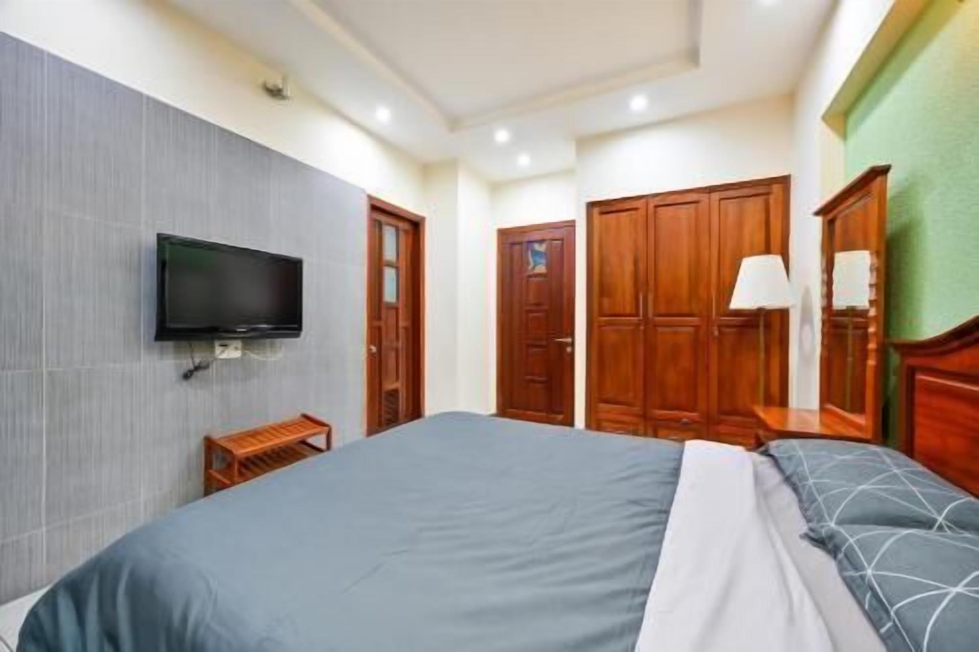 A hotel room with a bed, a TV mounted on the wall, wooden wardrobes, and a lamp.