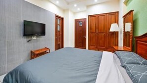 A hotel room with a bed, a TV mounted on the wall, wooden wardrobes, and a lamp.