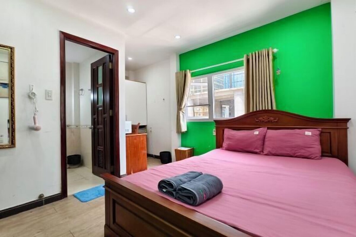Un dormitorio con cama, espejo, ventana con cortinas y pared verde.