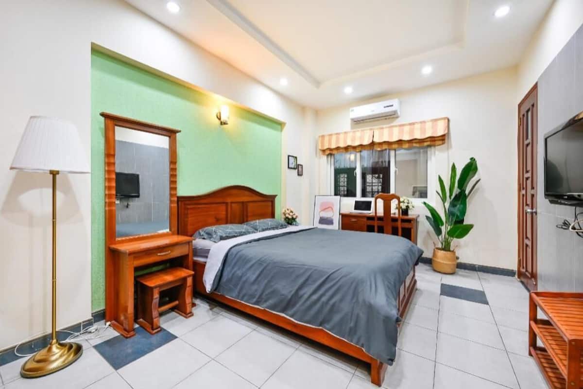A bedroom with a bed, bedside table, lamp, TV, and a potted plant.