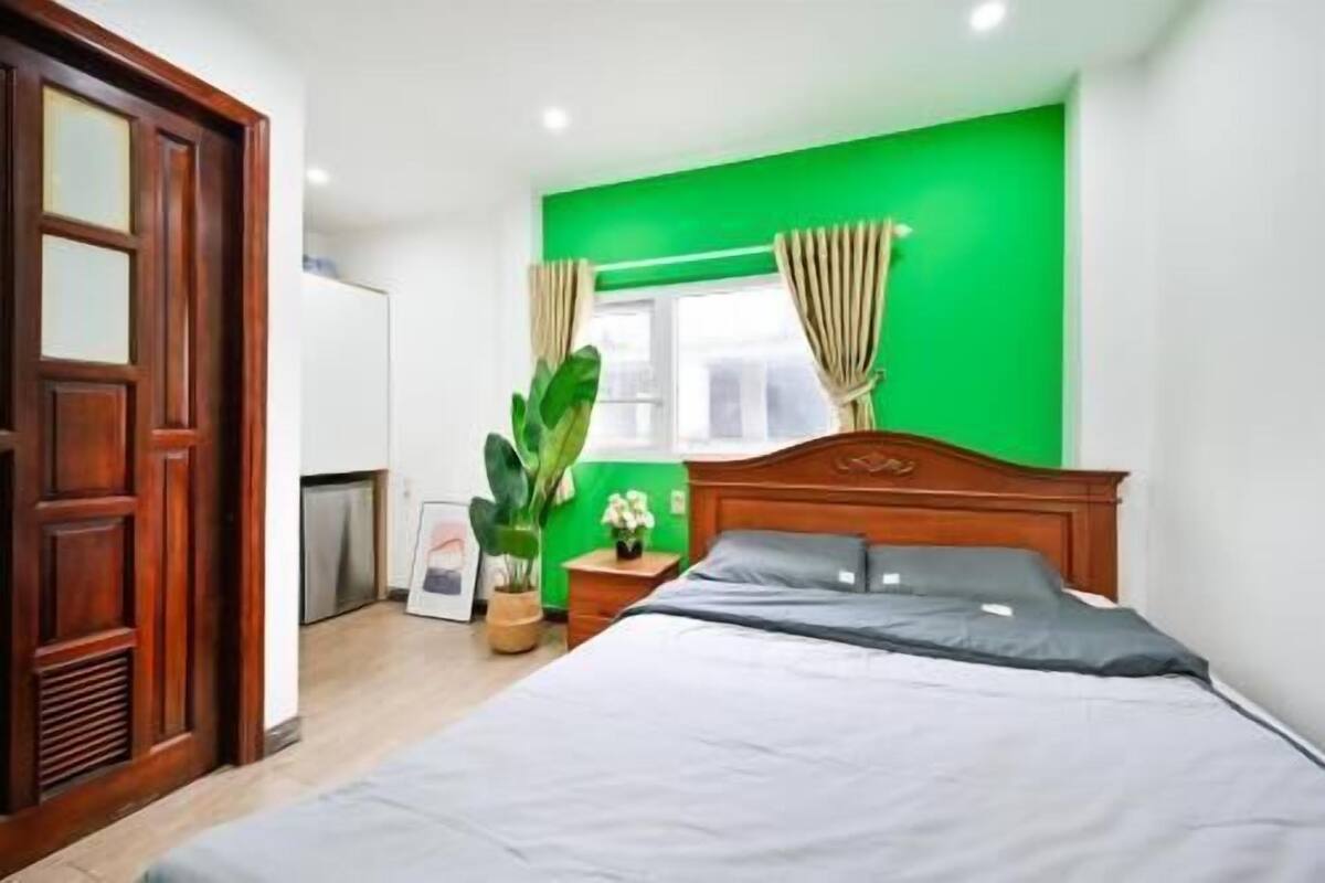 A bedroom with a bed, a nightstand, a potted plant, a window with curtains, and a green wall.