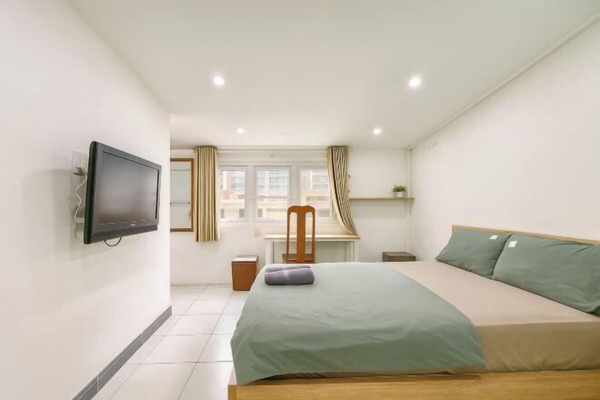 Ein Schlafzimmer mit einem Bett, einem an der Wand montierten Fernseher, einem Schreibtisch und einem Stuhl.