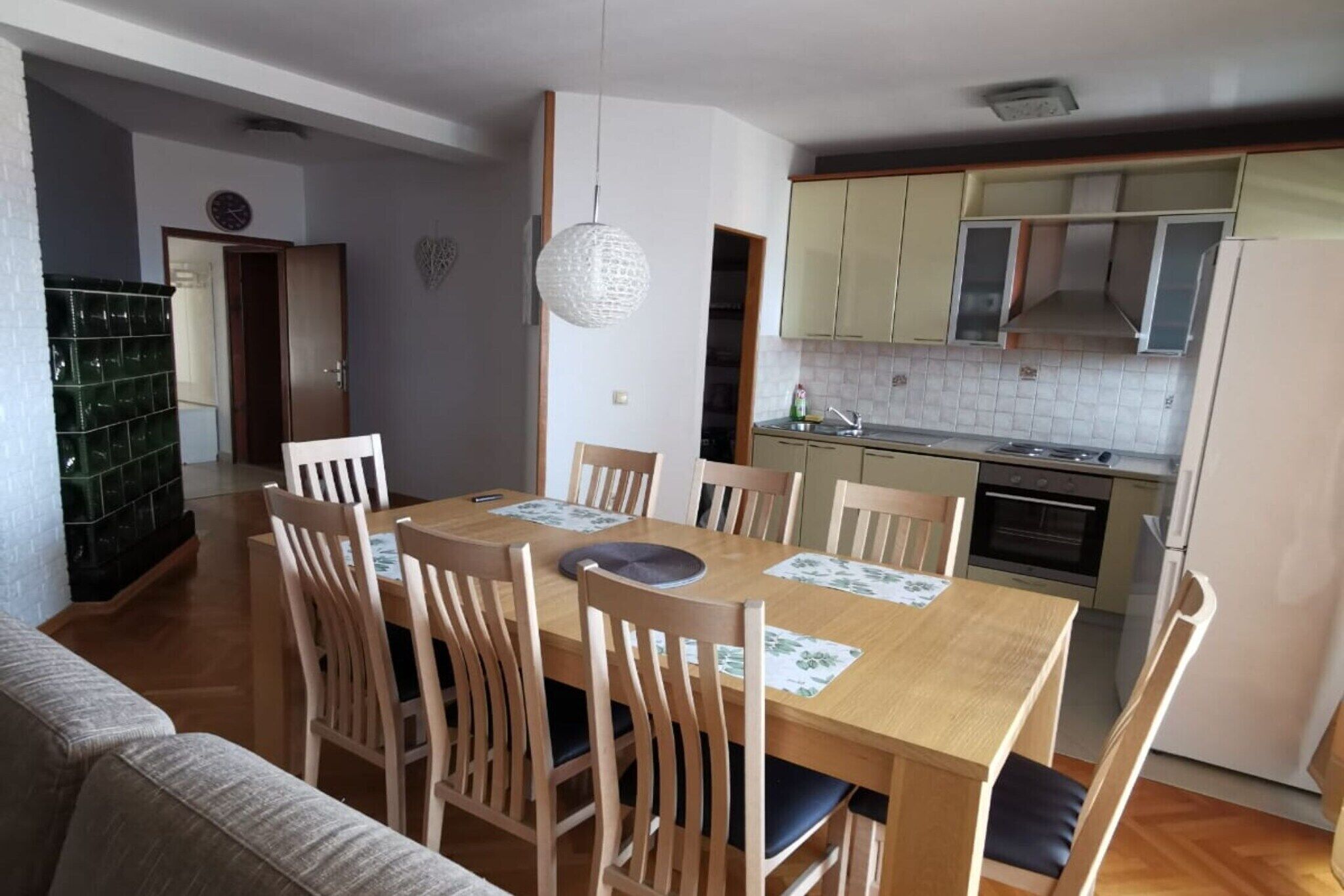 Un coin repas avec une table et des chaises en bois, un luminaire suspendu, et une cuisine équipée d’armoires et d’appareils électroménagers.