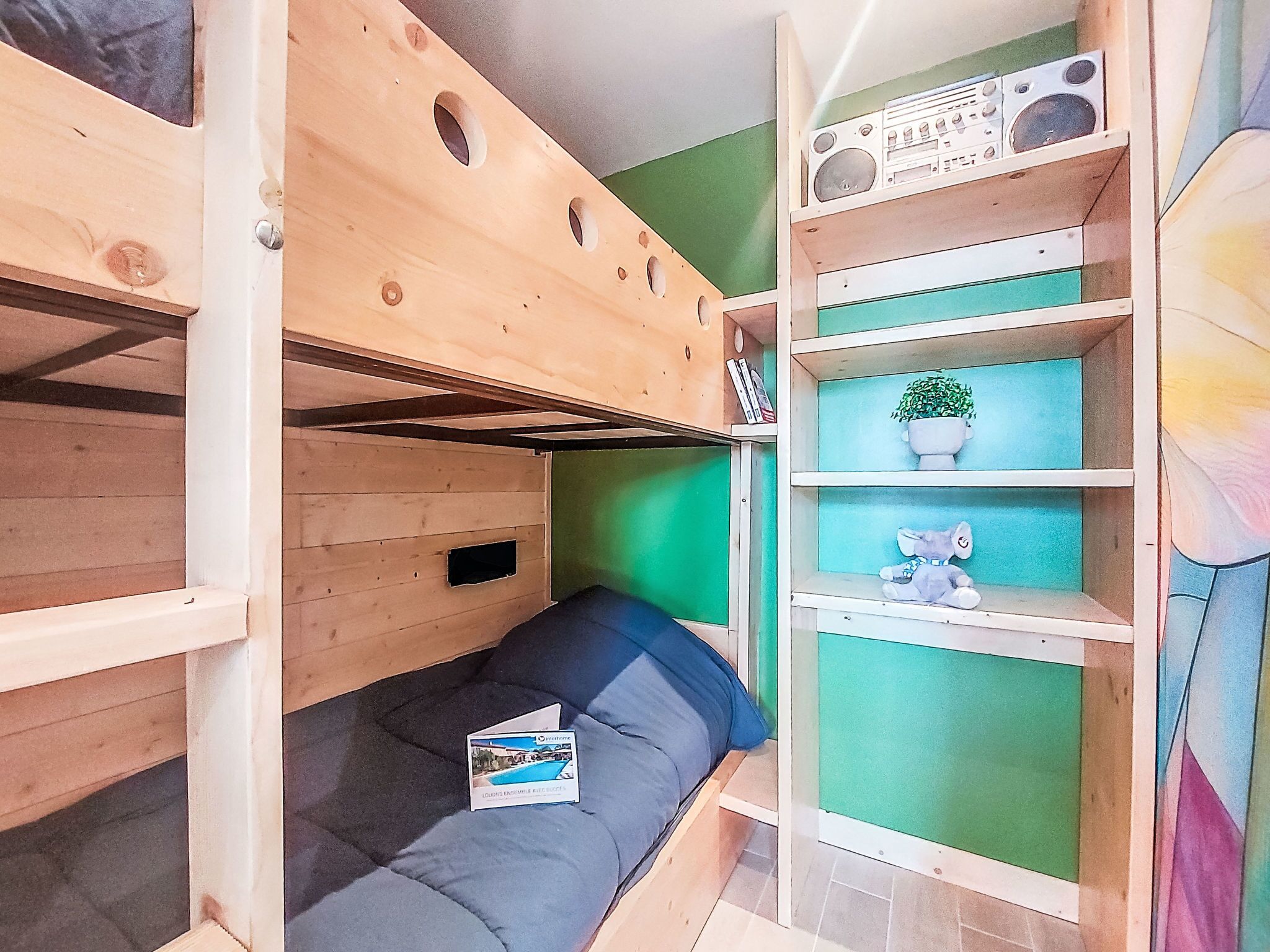 Ein Etagenbett mit Schreibtisch und Regalelement, ein Blumentopf und ein Stofftier.