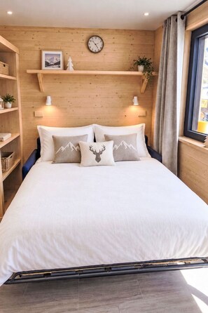 A bedroom with a wooden headboard, a bed with white bedding, decorative pillows, a wall clock, and a window with curtains.