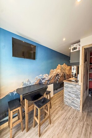 Una cocina moderna con un mural de montañas, taburetes de madera, una encimera negra y un televisor de pantalla plana montado en la pared.