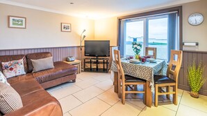 A cozy living room with a sofa, TV, dining table, and chairs. - Frobost Lodge by Interhome (South Uist)