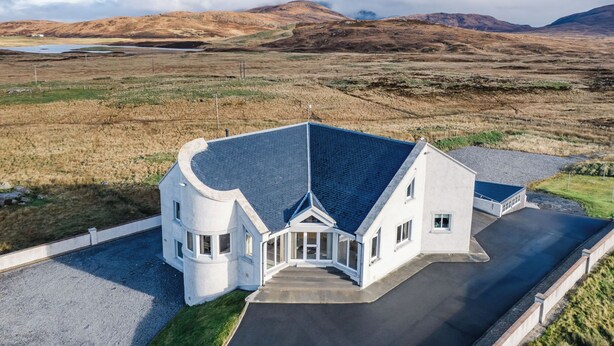 A modern house with a unique curved design, a large driveway, and a view of the surrounding landscape. - Frobost Lodge by Interhome (South Uist)