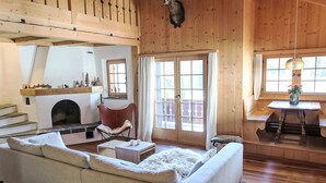 A cozy cabin interior with a sofa, fireplace, wooden walls, and a dining area.