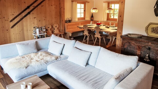A cozy wooden interior with a light-colored sofa, wooden dining table, and a rustic wooden chest.