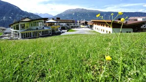 Et hotel med flere bygninger, en parkeringsplads og et bjerglandskab i baggrunden.
