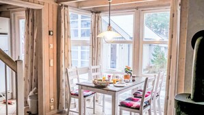 Comedor con una mesa dispuesta para cuatro, sillas blancas y una lámpara colgante.