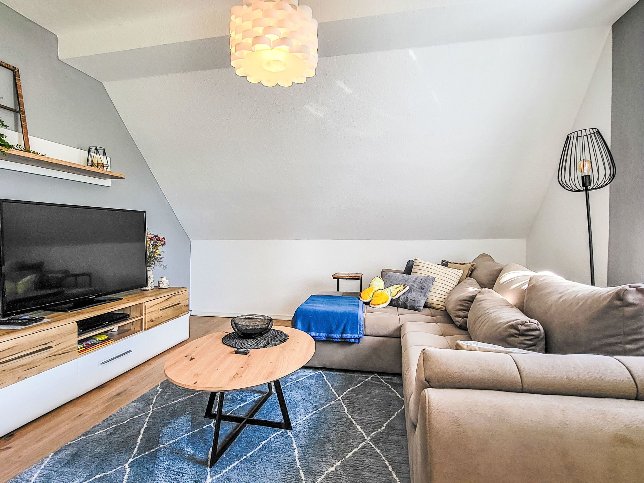 Un salon moderne doté d’un téléviseur à écran plat, d’un meuble de rangement en bois et d’un tapis bleu à motifs.
