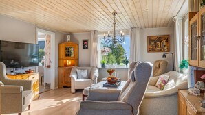 A cozy living room with a wooden ceiling, a television, a wooden cabinet, and a comfortable seating area with a sofa and armchairs.