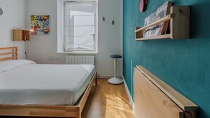 A bedroom with a bed, a window, a radiator, a wall-mounted shelf, and a floor lamp.