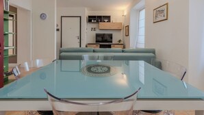 A modern living room with a glass dining table, a sofa, a TV, and a bookshelf.