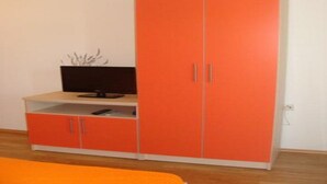 Ein Zimmer mit einem großen, orangefarbenen Kleiderschrank, einem Fernseher auf einem weißen Regal und einer kleinen Pflanze.