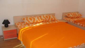 Habitación de hotel con dos camas, cada una con ropa de cama naranja y almohadas a juego. Se observa una mesita de noche con una lámpara y un mueble cajonero rojo.