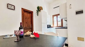 Eine Küche mit weißen Schränken, einer Holztür, einer Mikrowelle und einem Fenster.