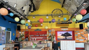 Een gezellig bar met houten meubels, een groot scherm waarop een strandafbeelding staat, en diverse borden en decoraties.