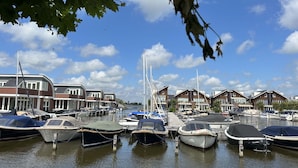 Een jachthaven met verschillende boten die aanmeren, omringd door moderne huizen met grote ramen en een heldere blauwe lucht.