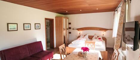 Une pièce chaleureuse avec un plafond en bois, un canapé rouge, une table à manger avec des chaises et un lit avec un téléviseur fixé au mur.
