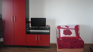 A room with a red wardrobe, a black TV on a black stand, and a bed with a red rose-patterned bedspread. - Apartments Višnja -  Standard One Bedroom Apartment (Klek)