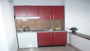 A compact kitchen with red cabinets, a white dishwasher, a sink, and a kettle. - Apartments Višnja -  Standard One Bedroom Apartment (Klek)