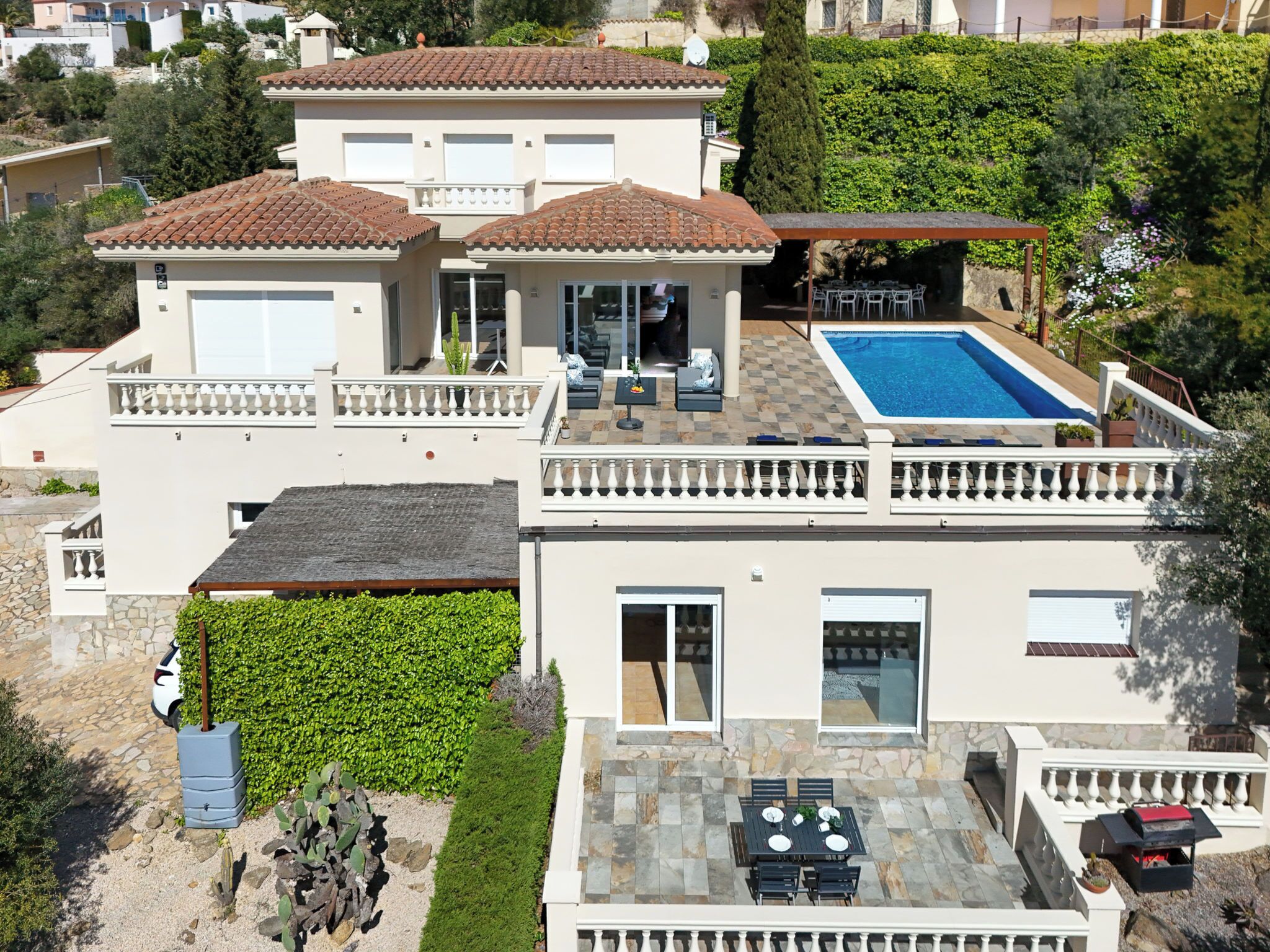 A two-story house with a swimming pool, a patio with outdoor furniture, and a well-maintained garden.