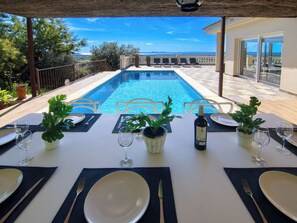 Ein Esstisch für zwei Personen mit Blick auf einen Swimmingpool und eine weite Landschaft.