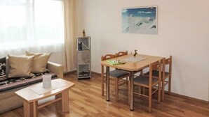 Ein Wohnzimmer mit Sofa, einem kleinen Tisch, einem Esstisch mit Stühlen, einem Bücherregal und einem Gemälde an der Wand.
