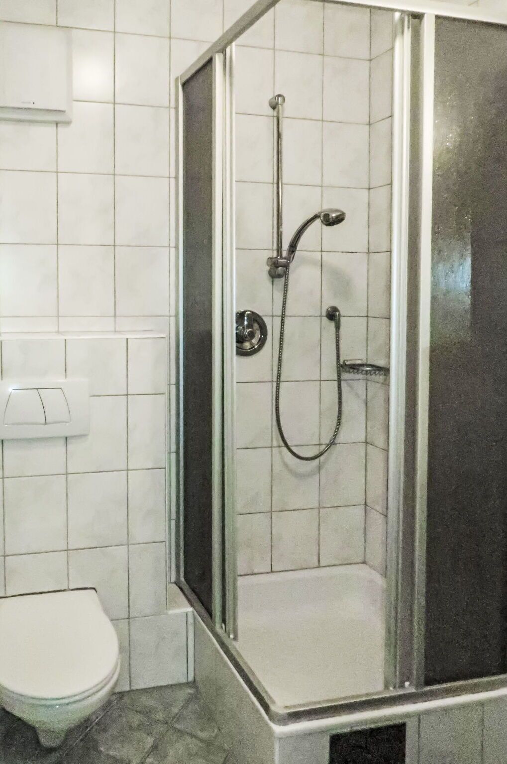 A bathroom with a glass-enclosed shower, a toilet, and tiled walls.